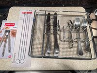 Overall lot: grill basket, packaged skewers, packaged nutcracker, flatware in basket