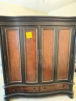 Front view of closed armoire showing two-tone finish, double doors, curved base and drawers