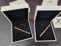 Both brooches in their original boxes with Swarovski cards visible