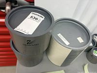 Two Swarovski cylindrical boxes with labels and MaxSold tag