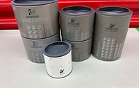 Five Swarovski cylindrical boxes: four grey Silver Crystal tubes, one white SCS tube