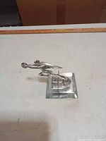 Front angle of metal hood ornament on clear base