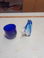 Blue glass cup and dolphin figurine side by side, showing color and shape
