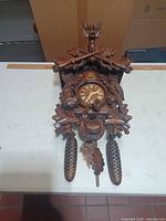 Front view of carved hunter motif cuckoo clock with two pinecone weights and chains visible