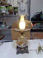 Full view lit showing amber upper globe, clear lower globe, ornate metal base and cord