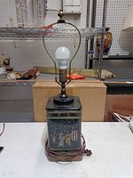 Front view showing full lamp, painted tin base, cord, harp, bulb