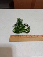 Front view of green glass horse paperweight beside ruler