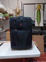 Front view of black Swiss Gear rolling suitcase showing logo, zip pockets, overall condition