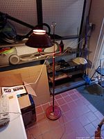 Full view of red metal floor lamp showing base, pole, arms, shade, and cord