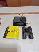 Front view of Bushnell 8x21 binoculars, case, instruction booklet