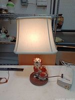 Front view of lit lamp showing shade, ceramic dog figurine, wooden base, power cord