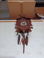 Front view of wooden cuckoo clock with carved leaves, bird, dial visible, chains hanging