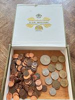 Open cigar box showing pennies on left and assorted dollar coins on right