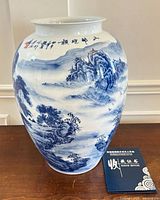 Front view of tall blue and white porcelain landscape vase with certificate booklet