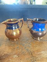 Both copper lusterware creamers side by side front view