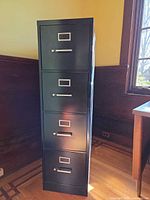 Front view of black 4-drawer filing cabinet showing handles and label frames