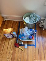 Overall lot showing metal trash can, tote with cleaners, brushes on floor