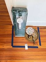 Box containing Howard Miller Emmett 625-514 wall clock, mosaic plate and metal plate on floor