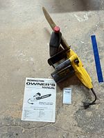 Chainsaw with bar cover, oil bottle, and owner’s manual laid out on floor