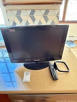 Front view of Samsung 19-inch LCD TV on stand with remote and antenna visible