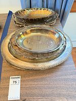 Stacked silver-plated pieces showing large round tray, oval platters and round dish