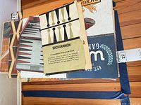 Stack showing backgammon instruction booklet, partial view of game boxes