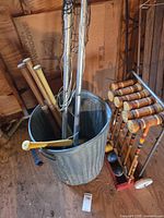 Galvanized trash can filled with bats and poles next to croquet stand with mallets and balls
