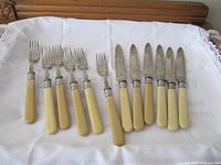 Set of six fish knives and six matching forks with cream faux bone handles laid out on cloth