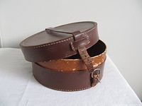 Closed and partially open view of brown leather collar box showing strap buckle and interior wear