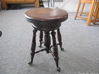 Full view of solid wood piano stool showing round seat, turned legs, brass claw glass ball feet
