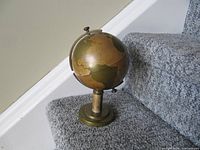 Closed brass globe cigarette dispenser on pedestal