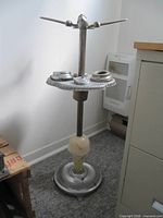 Full view of vintage metal smoker's stand showing airplane finial, four ashtray compartments, glass lighted section, and base