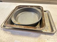 Stacked view showing square pan with rust nested in cookie sheet with round pan on top