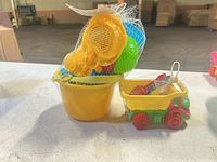 Entire sand toy set sealed in netting showing bucket, sieve, scoop, dump truck and contents