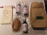 Complete lot showing three oil bottles in bubble wrap, wooden brush in plastic, drawstring pouch, brown paper bag