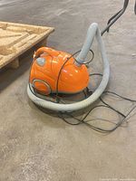 Orange Hoover canister vacuum with hose and power cord visible