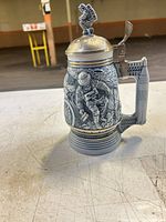 Front view of gray and blue beer stein showing astronaut relief and pewter lid