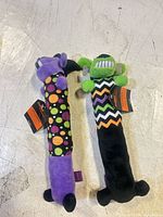 Front view of both plush dog toys showing colors, patterns, and attached tags