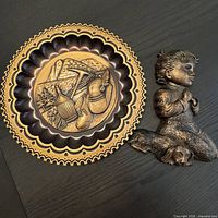 Round copper-tone wall plate alongside praying boy plaque