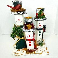 Front view of three wood snowman candle holders with decorations