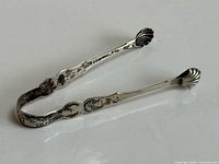 Full view of sterling silver tongs showing scallop tips and engraved arms