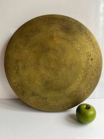Front view of brass gong next to apple for scale