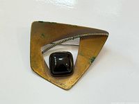 Front view of brass triangular brooch showing dark cabochon and tarnish