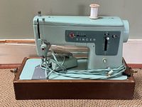 Front angled view showing turquoise Singer 337 sewing machine on wood base with foot pedal and cords