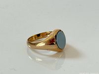 Side view of gold signet ring showing blue-grey stone and band profile