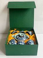 Open green box showing teapot and five cups in yellow lining