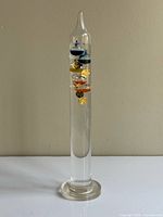 Full front view of entire glass Galileo thermometer on base