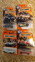 Four sealed Matchbox die-cast car packages on woven surface