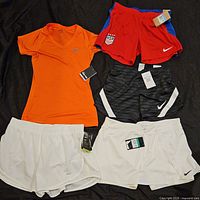 All five Nike garments laid out: orange tee, red USA shorts, black shorts, two white shorts