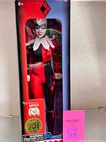 Front view of boxed Harley Quinn figure showing outfit, face sculpt, hologram seal, and Mego branding